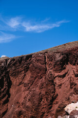 Huge red rock cliff on red sand beach Santorini. Alien landscape.