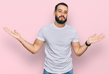 Young man with beard wearing casual white t shirt clueless and confused expression with arms and...