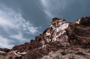 Huge red and yellow rock cliff on red sand beach Santorini. Alien landscape.