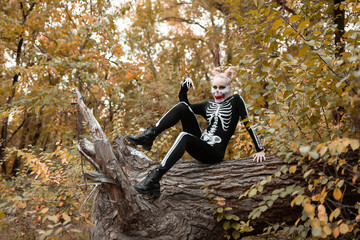 A girl with a scary make-up in a skeleton costume, a mask with rhinestones in a gloomy autumn...