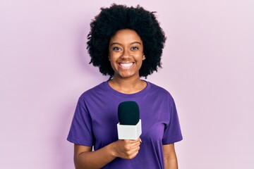 Young african american woman holding reporter microphone smiling with a happy and cool smile on face. showing teeth. - obrazy, fototapety, plakaty