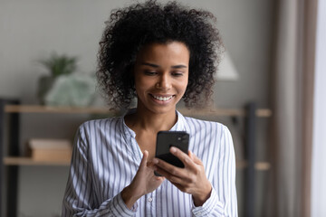Fototapeta na wymiar Entertainment app. Afro american female teenager student using smartphone for chatting networking online playing games. Young mixed race woman messaging dating on phone buying goods via internet order