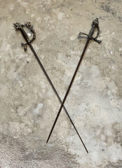 Two swords hang on an old gray wall on a castle. The swords cross.