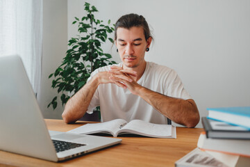 Pensive student making notes from laptop. Young man studying at home and prepare for pass exam