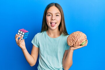 Beautiful brunette little girl playing colorful puzzle cube intelligence game and holding brain...