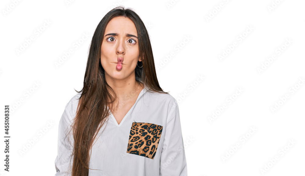 Sticker young hispanic girl wearing casual clothes making fish face with lips, crazy and comical gesture. fu