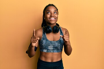 African american woman with braided hair wearing sportswear and arm band amazed and surprised looking up and pointing with fingers and raised arms.