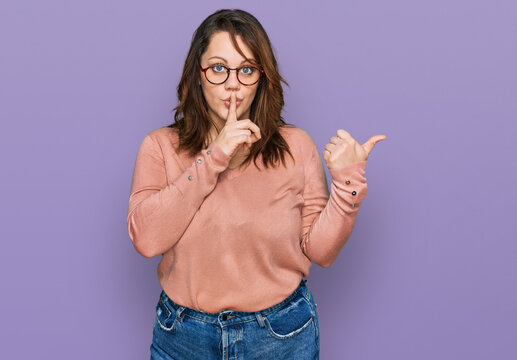 Young plus size woman wearing casual clothes and glasses asking to be quiet with finger on lips pointing with hand to the side. silence and secret concept.