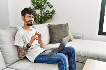 Hispanic man with beard sitting on the sofa disgusted expression, displeased and fearful doing...