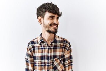 Hispanic man with beard standing over isolated background looking away to side with smile on face, natural expression. laughing confident.