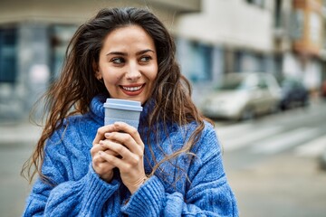 Young hispanic woman smiling happy smelling coffee at the city.