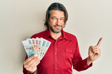 Middle age handsome man holding czech koruna banknotes smiling happy pointing with hand and finger to the side