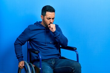 Handsome hispanic man with beard sitting on wheelchair feeling unwell and coughing as symptom for cold or bronchitis. health care concept.