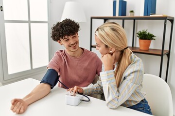 Young couple smiling happy measuring blood pressure using tensiometer at home.