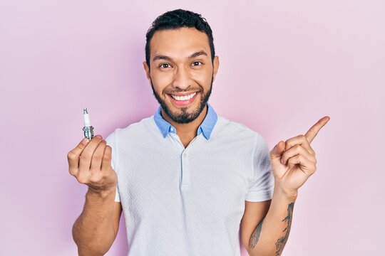 Hispanic man with beard holding spark plug smiling happy pointing with hand and finger to the side