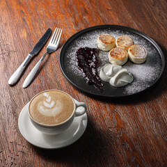From above of cup with cappuccino coffee and plate with cheese pancakes placed on wooden table with knife and fork for nutritious breakfast 