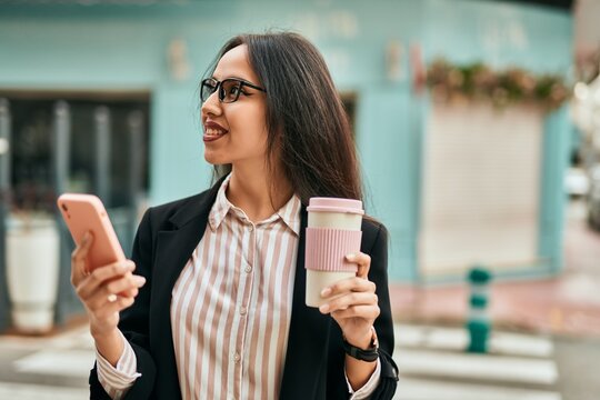 Young hispanic businesswoman using smartphone drinking coffee at the city.