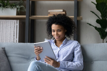 Using pad. Smiling african american woman enjoy watching video read ebook surf social media chat on...