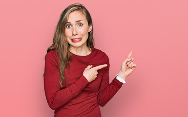 Young blonde woman wearing casual clothes pointing aside worried and nervous with both hands,...