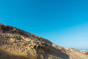 Yellow sandstone sedimentary texture and weathering under the blue sky with many small caves on the rocky coast