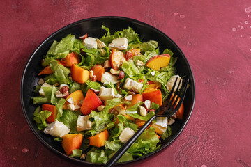 Salad with cheese and peach on a black plate