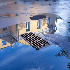 Reflection of blue skies and houses in a puddle after rain