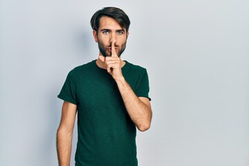 Young hispanic man wearing casual white tshirt asking to be quiet with finger on lips. silence and secret concept.