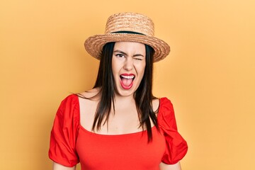 Young hispanic woman wearing summer hat winking looking at the camera with sexy expression, cheerful and happy face.