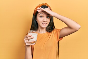 Young brunette girl drinking a glass of milk stressed and frustrated with hand on head, surprised...