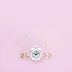 Obraz na płótnie Canvas Аlarm clock and numbers 2022 are decorated with golden star confetti on pink background. Minimal concept of celebrating Christmas and New Year. Square orientation