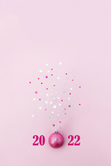 Christmas ball sparkles with star confetti on pink background. Minimal concept of 2022 New Year. Vertical banner, copy space