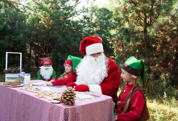 Cute little kids sit at a table against the backdrop of the forest in elven and santa costumes for Christmas and New Year with room for text. Holiday concept