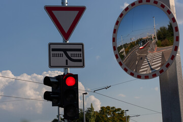 Un feu rouge avec un c&eacute;dez le passage et un miroir dans lequel se refl&egrave;te le tramway qui arrive