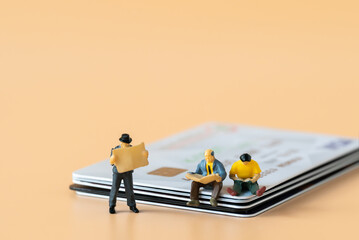 Miniature people figures Businessman sitting and reading Financial book or newspaper on credit card with copy space using as Success Business development and Blockchain Commerce Strategy Planning 