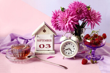 Calendar for September 3 : the name of the month in English, cubes with the numbers 0 and 3, a bouquet of pastel dahlias, raspberries in a cup, an alarm clock, a cup of fragrant tea