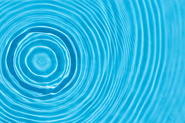 Wave from a drop of water on blue water under natural light. Top view, flat lay