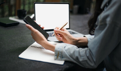 Focus on hand young asian woman holding pen and using mobile phone working with computer laptop on counter bar in coffee shop