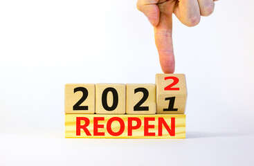 2022 reopen new year symbol. Businessman turns a wooden cube and changes words 'Reopen 2021' to...