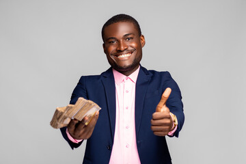 excited and happy young african man holding out a lot of money and doing a thumbs up