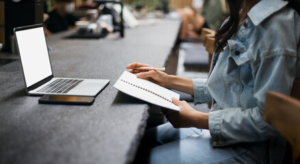 Focus on hand young asian woman reading an appointment in book while she working with computer laptop on counter bar in coffee shop