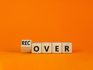 Time to recover symbol. Turned a wooden cube and changed the word 'over' to 'recover'. Beautiful orange table, orange background. Business, over or recover concept. Copy space.