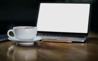 Focus on white coffe cup with computer laptop, note book on wooden table, dark tone