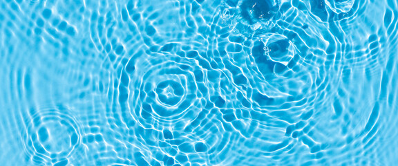 Wave from a drop of water on blue water under natural light. Top view, flat lay. 