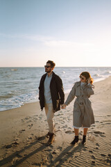 Young couple having fun walking and hugging on beach during autumn sunny day. Relaxation, youth, love,  lifestyle solitude with nature.