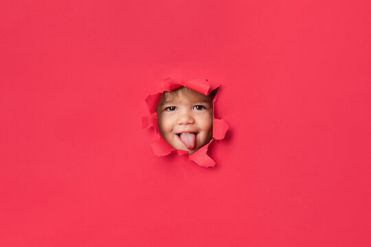 Funny little girl's face peeking through pink paper sticking tongue