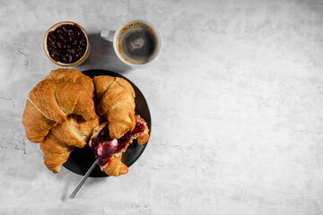 Fresh french croissant with cherry jam on grey plate and cap of fresh coffee on gray background,...