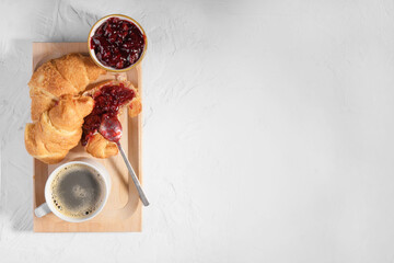 Fresh french croissant with cherry jam on wooden plate and cap of fresh coffee on gray background,...