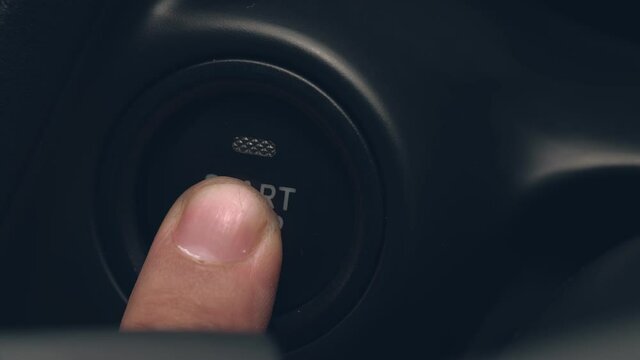 Close up of finger pressing the start-stop engine button on the car.
