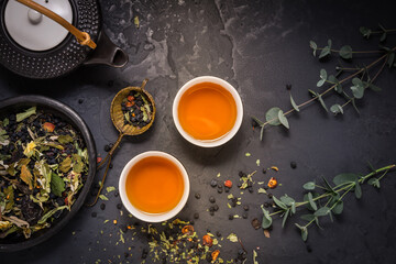 Obraz na płótnie Canvas Herbal tea with teapot and herbal leaves on black stone background