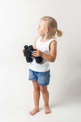 Blond child with binoculars on a light background in the studio